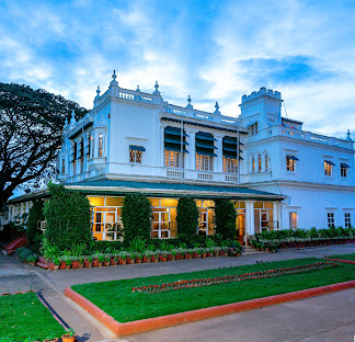 The Green Hotel, Mysuru: the white heritage building and lawn at dusk